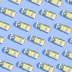 Geldscheine liegen symetrisch gerollt auf blauem Untergrund