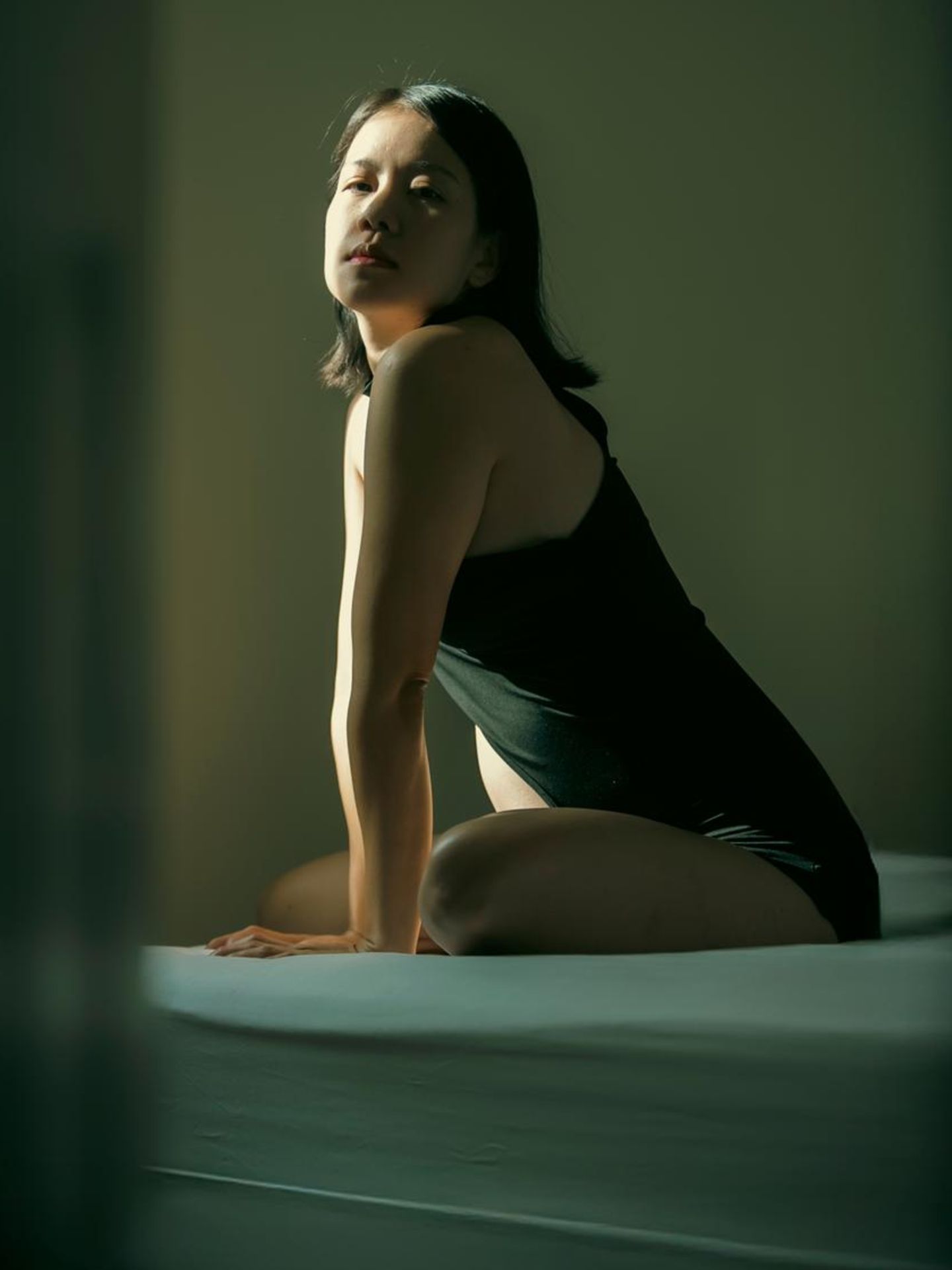 Fehlgeburt: eine Frau sitzt im halbschatten auf dem Bett und schaut in die Kamera