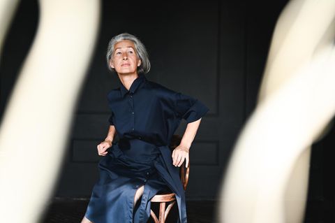 Eine ältere Frau sitzt auf einem Holzstuhl und schaut in die Ferne