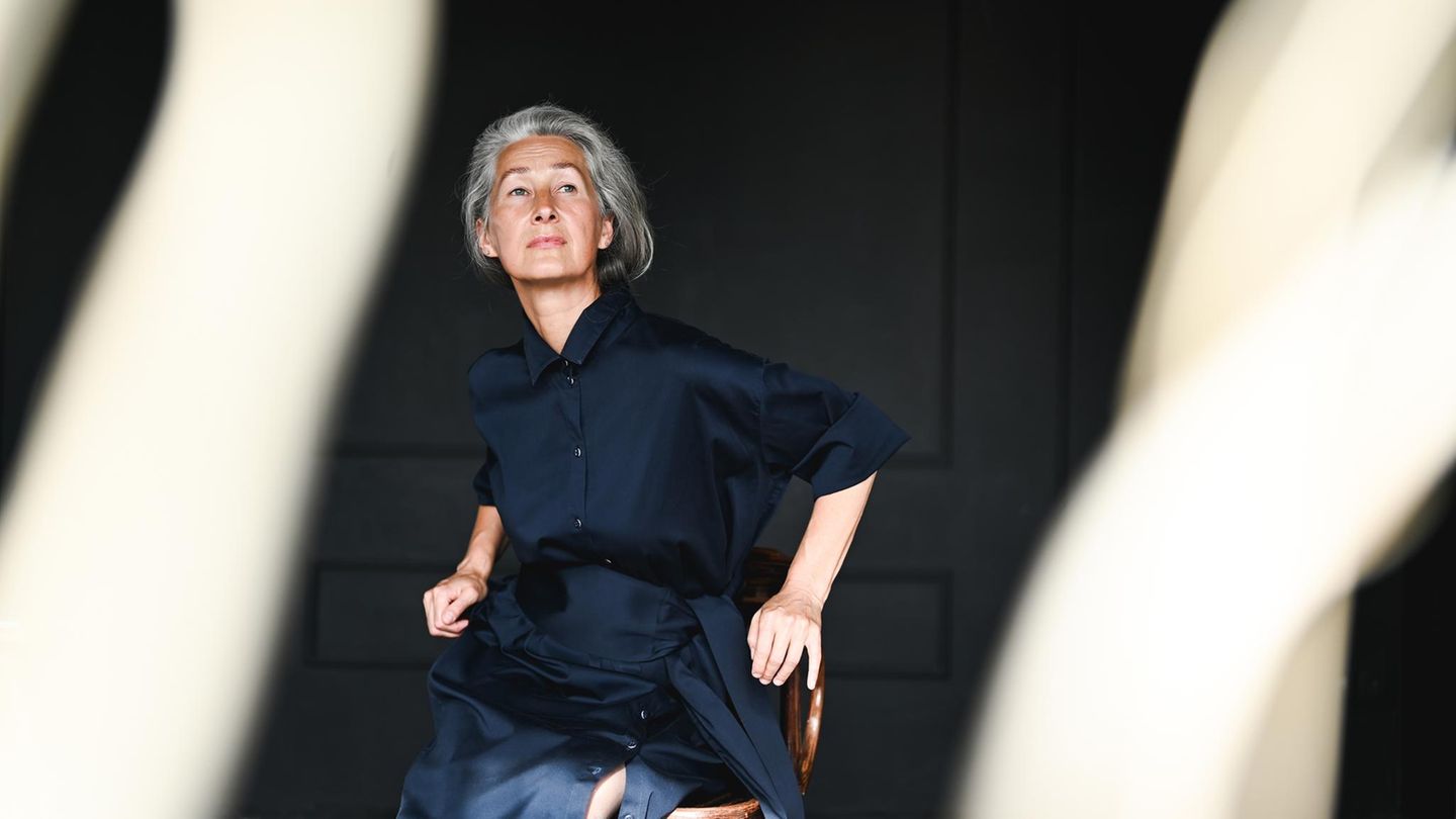 Eine ältere Frau sitzt auf einem Holzstuhl und schaut in die Ferne