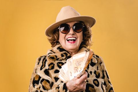 Frau mit Leo-Mantel, Sonnenbrille und Hut wedelt mit Geldscheinen - Symbolbild Rente Frau mit Leo-Mantel, Sonnenbrille und Hut wedelt mit Geldscheinen - Symbolbild Rente