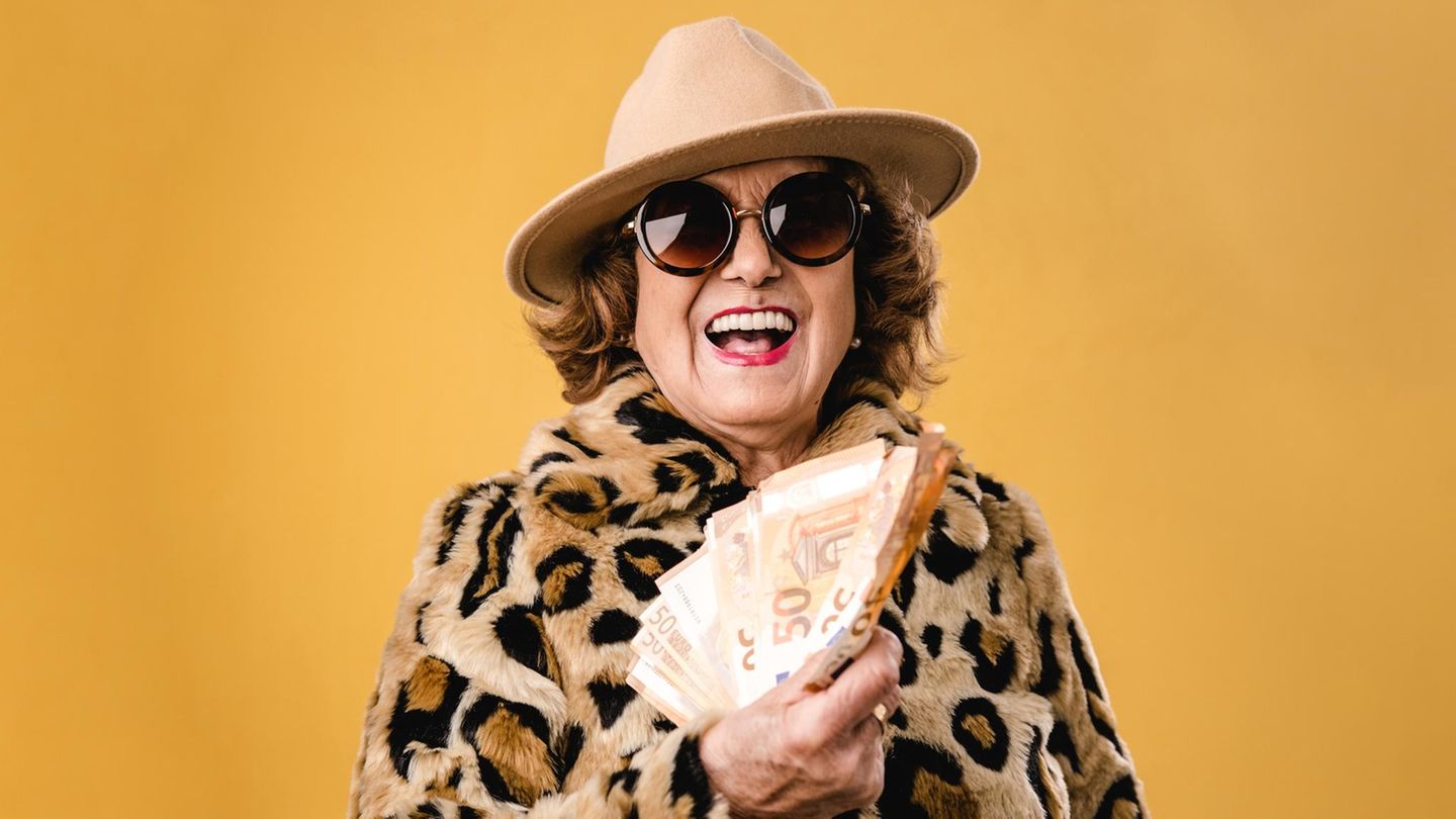 Frau mit Leo-Mantel, Sonnenbrille und Hut wedelt mit Geldscheinen - Symbolbild Rente Frau mit Leo-Mantel, Sonnenbrille und Hut wedelt mit Geldscheinen - Symbolbild Rente