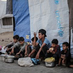 Kinder sitzen am Straßenrand in Gaza, vor ihnen stehen Töpfe