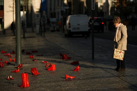 Stadtbild-Debatte (Symbolbild): Eine Frau schaut sich rot lackierte Schuhe auf der Straße an, ein Mahnmal