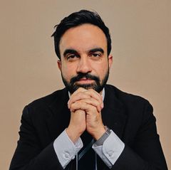 Zohran Momdani im Anzug vor einem neutralen Hintergrund