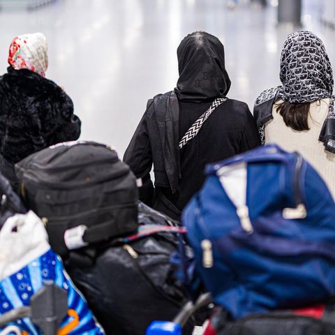 Drei Frauen aus Afghanistan gehen vor einem beladenen Gepäckwagen durch den Flughafen Hannover