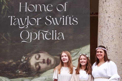 Fans stehen als Ophelia verkleidet vor einem Banner mit der Aufschrift "Home of Taylor Swifts Ophelia"