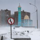 Ein blaues Gebäude sticht in der schneebedeckten Landschaft und den braunen Gebäuden hervor. In der Ferne eine Person