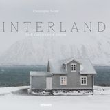 Ein Haus steht vor einem Fjord und einem schneebedeckten Hügel auf Island