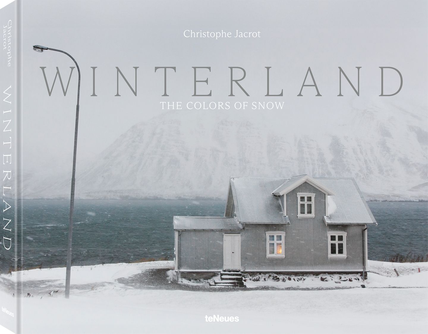 Ein Haus steht vor einem Fjord und einem schneebedeckten Hügel auf Island