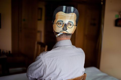 Ein Mann mit einer Maske auf dem Hinterkopf. Die Maske wirkt traurig