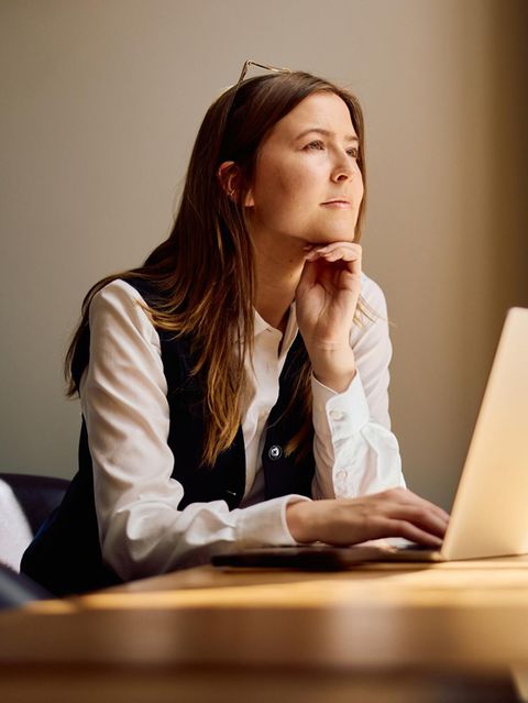 Symbolbild Unternehmensberaterin: Eine junge Frau sitzt am Laptop und schaut aus dem Fenster