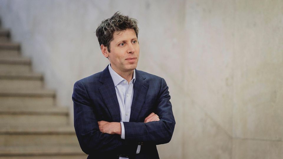 Sam Altman trägt Hemd und Sakko und steht mit verschränkten Armen in einem Treppenhaus