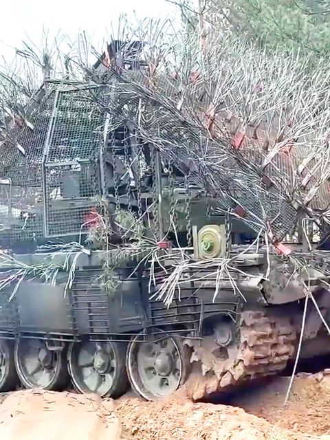 Ein russischer, mit abstehenden Drahtseilen verkleideter Panzer rollt über eine ländliche Straße.