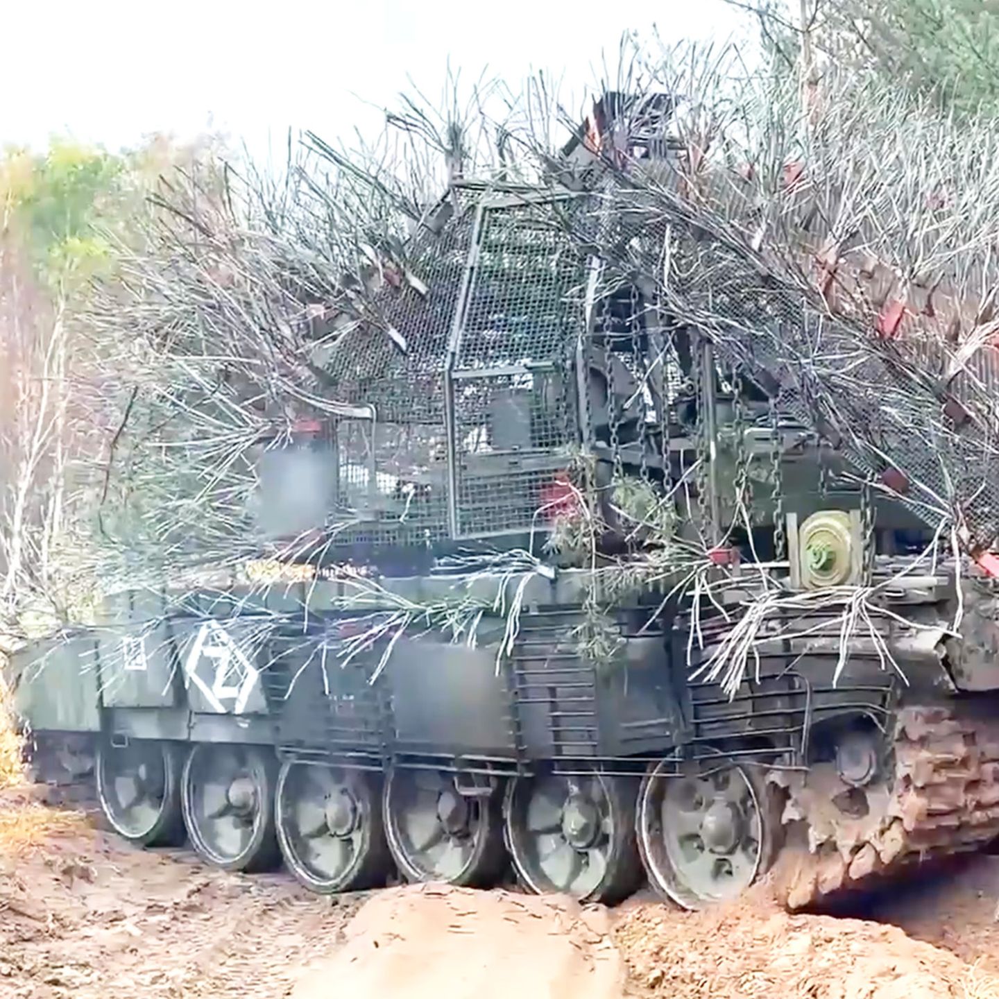 Ein russischer, mit abstehenden Drahtseilen verkleideter Panzer rollt über eine ländliche Straße.