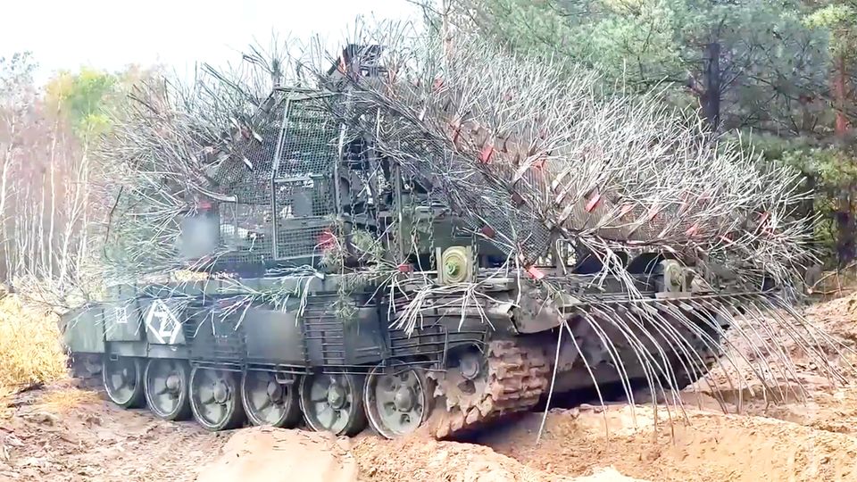 Ein russischer, mit abstehenden Drahtseilen verkleideter Panzer rollt über eine ländliche Straße.