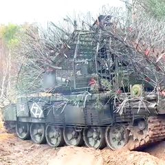 Ein russischer, mit abstehenden Drahtseilen verkleideter Panzer rollt über eine ländliche Straße.