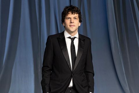 Jesse Eisenberg  steht in einem schwarzen Anzug vor einem grauen Hintergrund