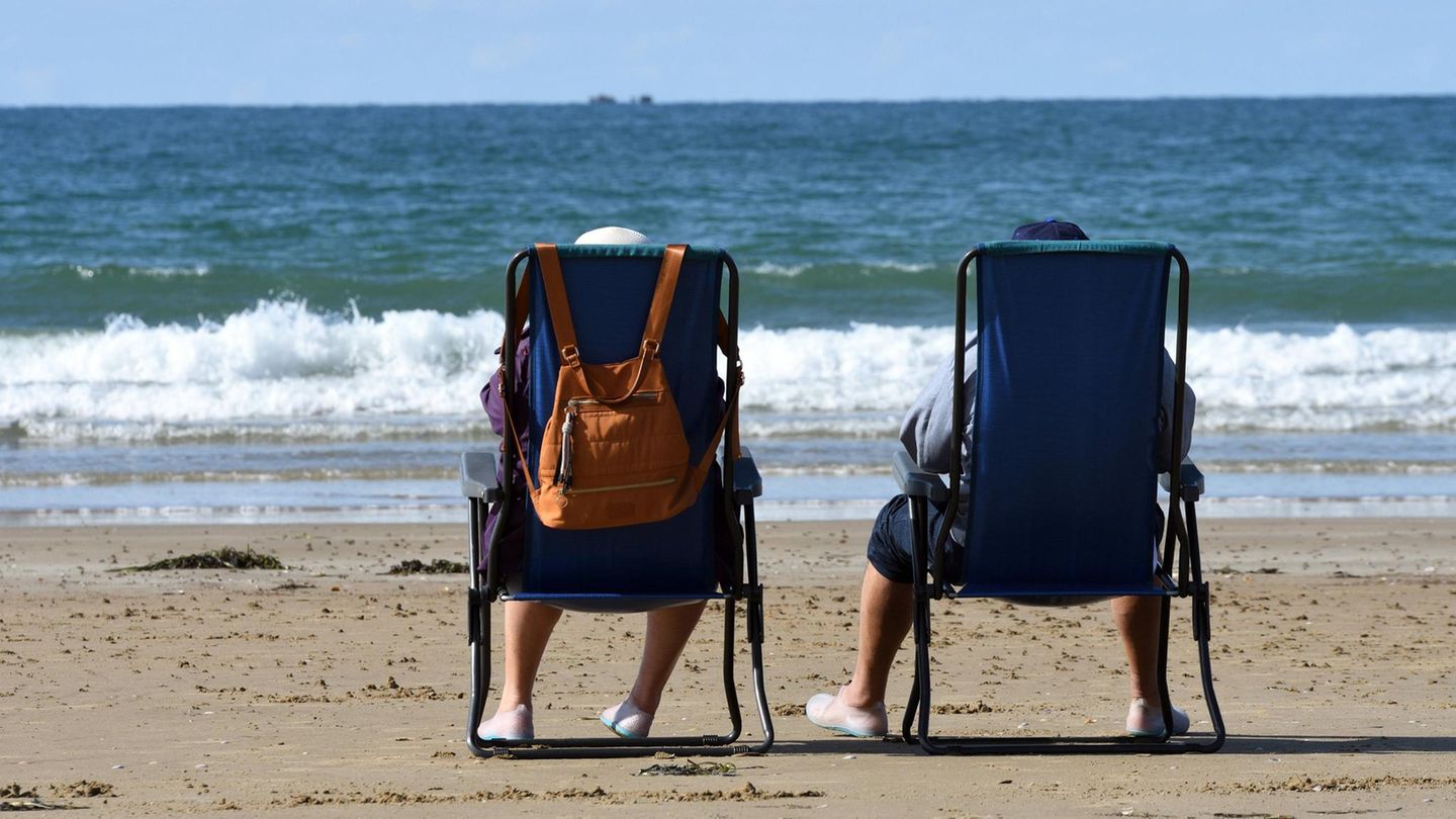 Ehepaar sitzt in Campingstuehlen am Strand und schaut aufs Meer