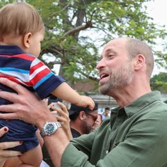 Eine Frau streckt Prinz William ihr Baby entgegen, er nimmt den Jungen entzückt auf den Arm.