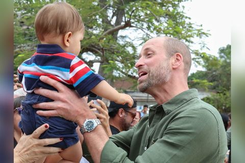 Eine Frau streckt Prinz William ihr Baby entgegen, er nimmt den Jungen entzückt auf den Arm.