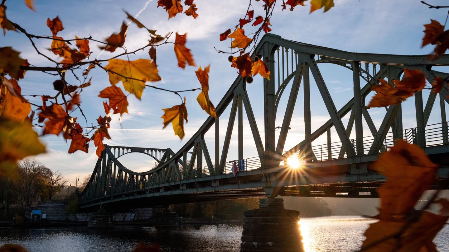 Potsdam, Deutschland. Ein Novembermorgen taucht die Glienicker Brücke in warmen Sonnenstrahlen. Orangefarbene und gelbe Blätter umrahmen dieses historische Symbol für deutsche Teilung und Wiedervereinigung