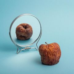 Abnehmspritze, Symbolbild: faltiger geschrumpfter Apfel vor eime Spiegel