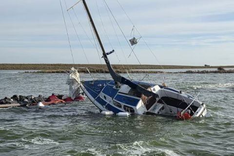 Ein kleines Segelboot liegt mit Schlagseite auf einem Steinwall an einer einsamen Insel im Ijsselmeer, Niederlande