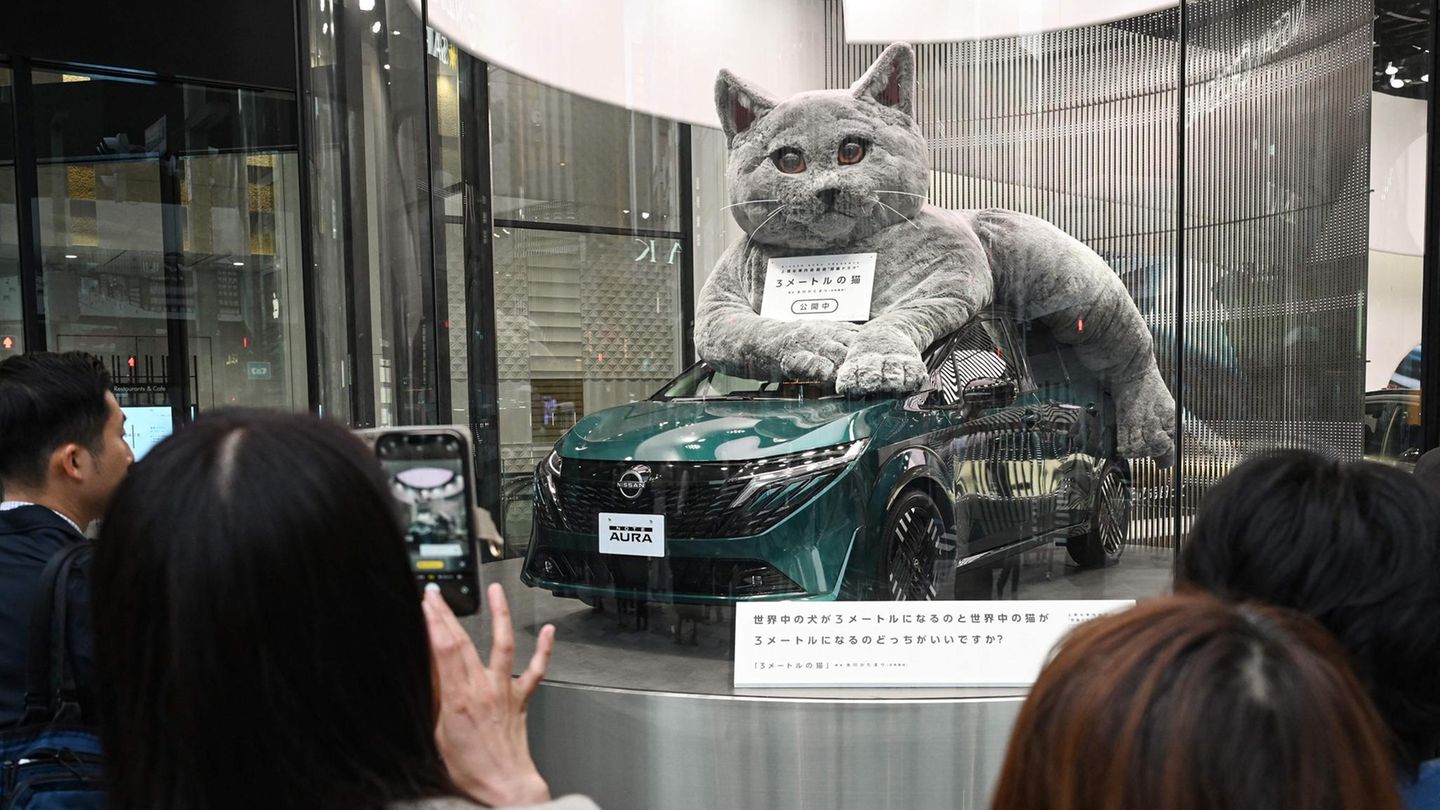 Tokio, Japan. In einem Showroom im luxuriösen Vergnügungsviertel Ginza hat es sich eine riesige Stoffkatze auf einem Nissan Note Aura bequem gemacht. Technik trifft Verspieltheit. Ob der Motor auch so schnurrt wie ein Kätzchen?