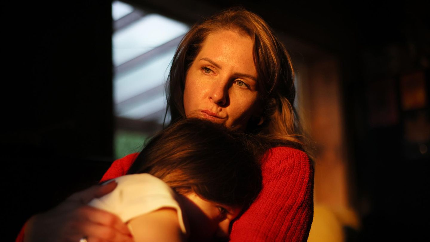 eine Frau, ein Elternteil, hält ihre Tochter im Halbschatten im Arm