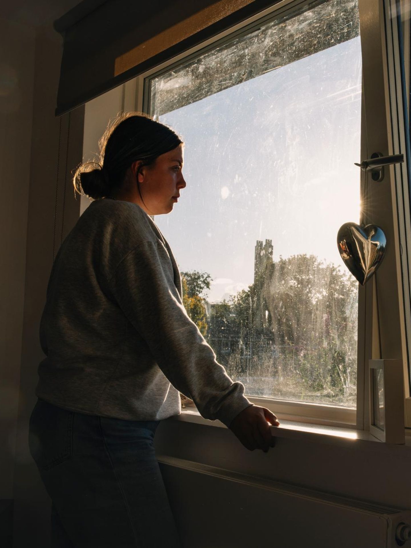 eine Frau in lockerer Kleidung steht am Fenster und schaut nachdenklich hinaus