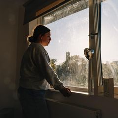 eine Frau in lockerer Kleidung steht am Fenster und schaut nachdenklich hinaus