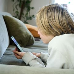 Ein Junge liegt auf einem Sofa und guckt auf sein Smartphone