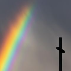 Ein kräftiger Regenbogen ist am dunklen Himmel neben dem Kreuz einer Kirche zu sehen
