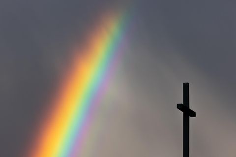 Ein kräftiger Regenbogen ist am dunklen Himmel neben dem Kreuz einer Kirche zu sehen