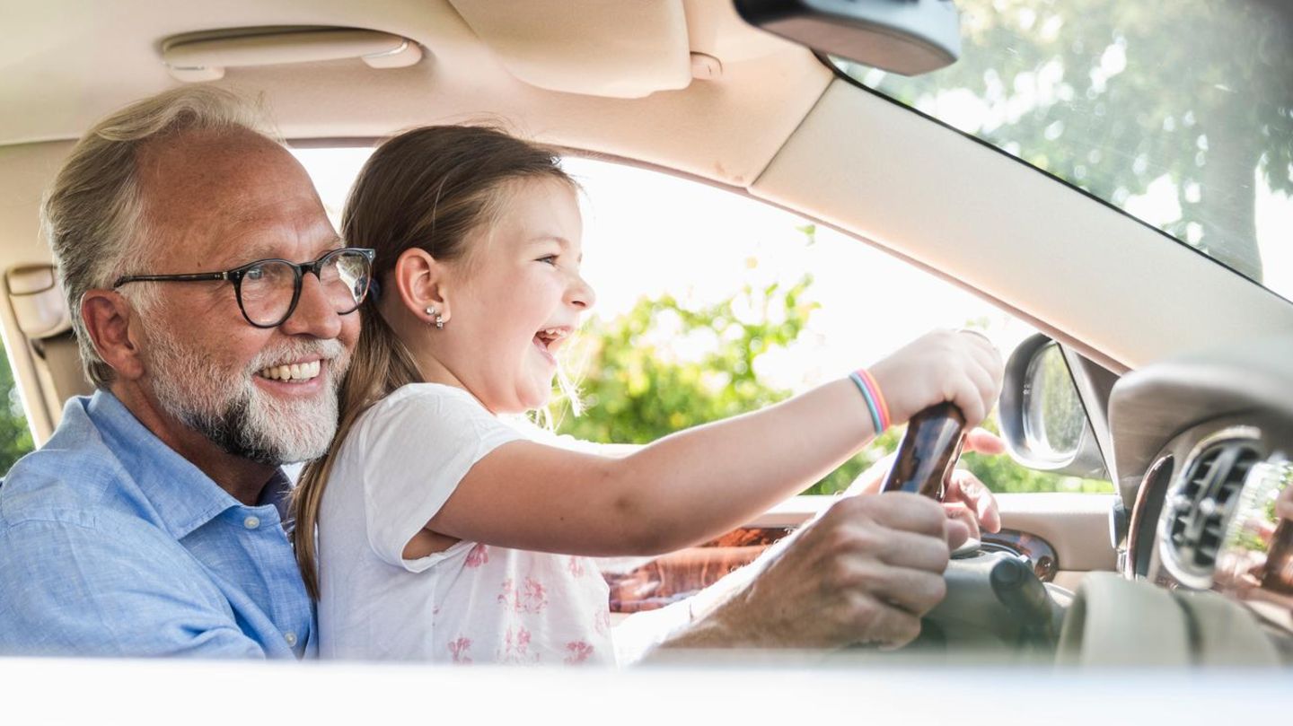 Mädchen sitzt beim Großvater auf dem Schoß am Steuer eines Autos – sie muss noch nicht in der Kfz-Versicherung abgedeckt sein