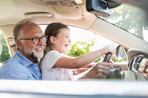 Mädchen sitzt beim Großvater auf dem Schoß am Steuer eines Autos – sie muss noch nicht in der Kfz-Versicherung abgedeckt sein