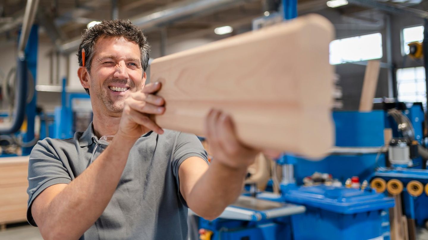 Zimmermann peilt über die Oberkante eine Bretts und macht einen glücklichen Eindruck – wegen des Gehalts?