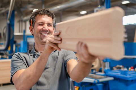 Zimmermann peilt über die Oberkante eine Bretts und macht einen glücklichen Eindruck – wegen des Gehalts?