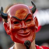 Ein Karnevalist mit einer roten Teufelsmaske steht auf der Straß