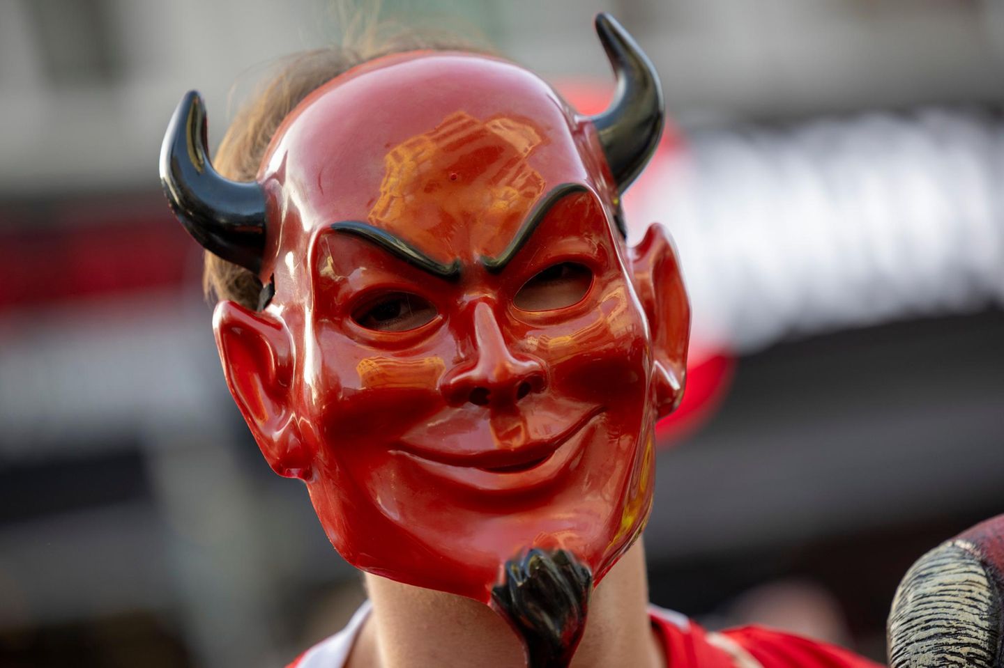 Ein Karnevalist mit einer roten Teufelsmaske steht auf der Straß