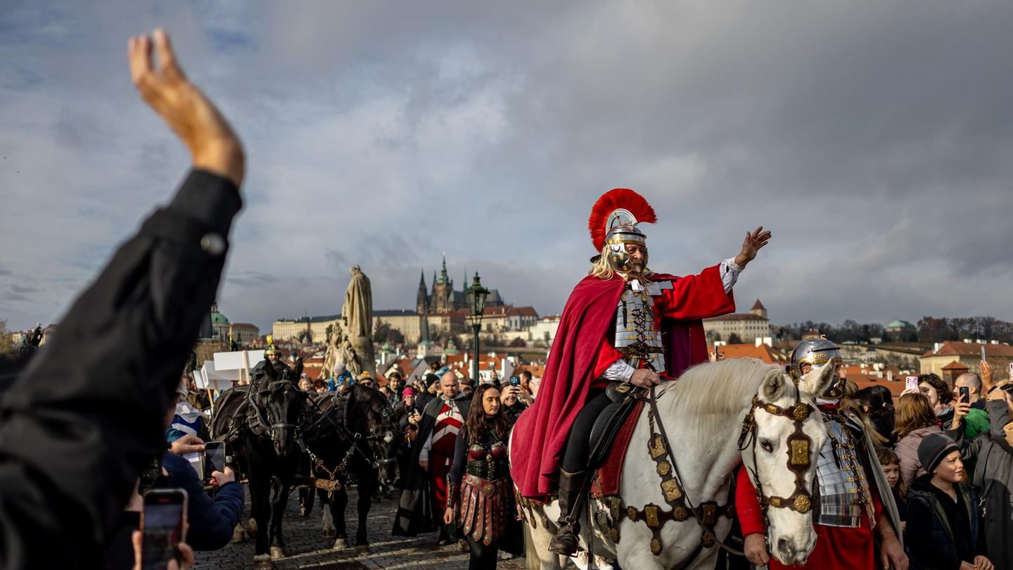 Prag, Tschechien. Ein als der heilige Martin von Tours verkleideter Mann reitet während einer Prozession auf der mittelalterlichen Karlsbrücke auf einem weißen Pferd. Die Ankunft des heiligen Martins auf einem weißen Pferd ist ein Volksbrauch, der mit dem Martinstag verbunden ist. Der Legende nach kündigt er den Winter und den ersten Schneefall an. In tschechischen Städten und Dörfern wird dieser Tag mit Laternenumzügen, Kostümaufführungen und dem Genuss von jungem Wein und Gänsebraten gefeiert, die den Überfluss und das Ende des landwirtschaftlichen Jahres symbolisieren