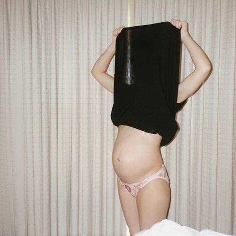 Kinderwunsch: Frau hebt ihr Shirt über den Kopf und zeigt ihren nackten Babybauch