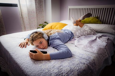Ein Mädchen liegt auf dem Bett und schaut auf das Handy