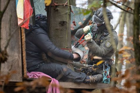 Ein Aktivist hat sich festgeklebt - ein Beamter des Höhen-Interventionsteams löst ihn ab. Foto: Boris Roessler/dpa