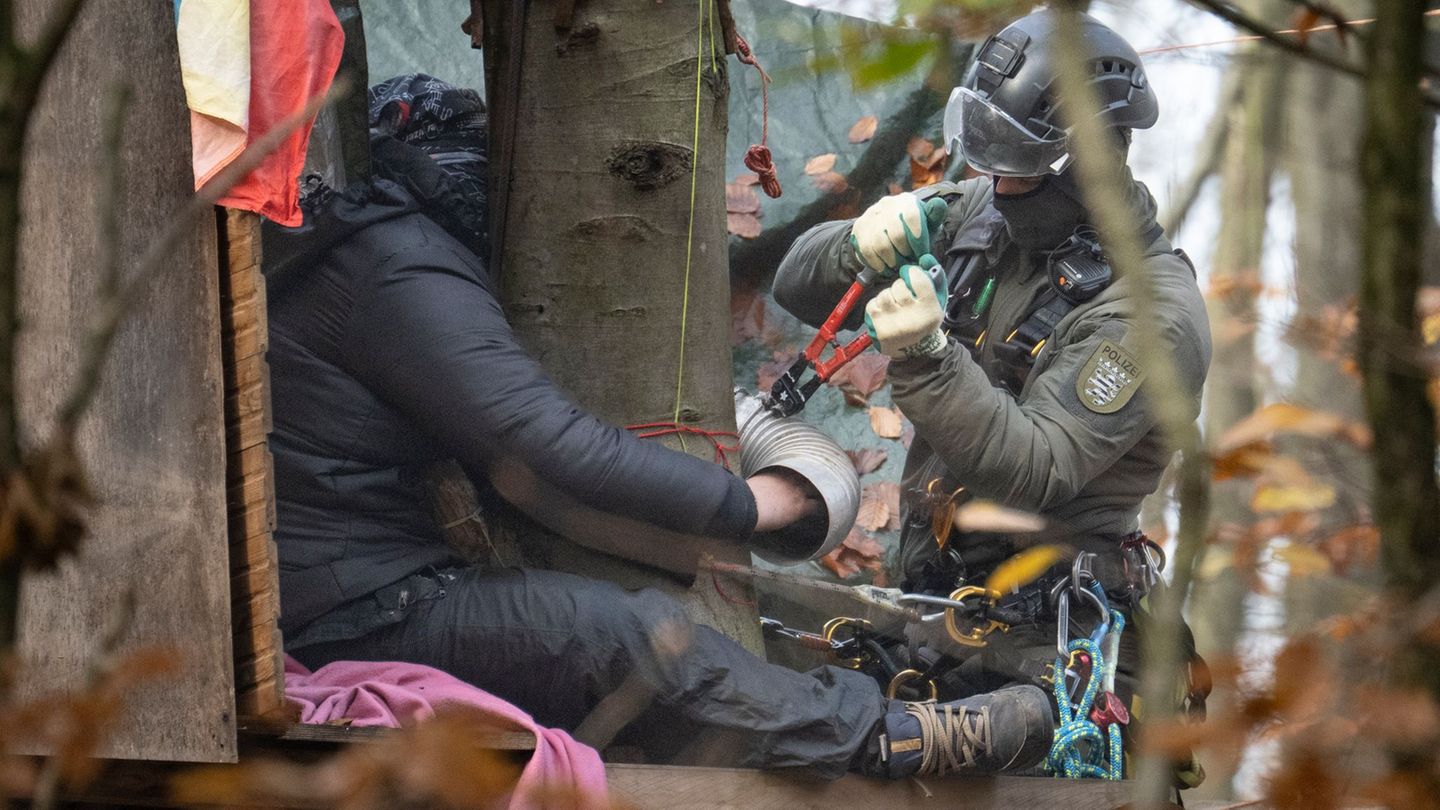 Ein Aktivist hat sich festgeklebt - ein Beamter des Höhen-Interventionsteams löst ihn ab. Foto: Boris Roessler/dpa