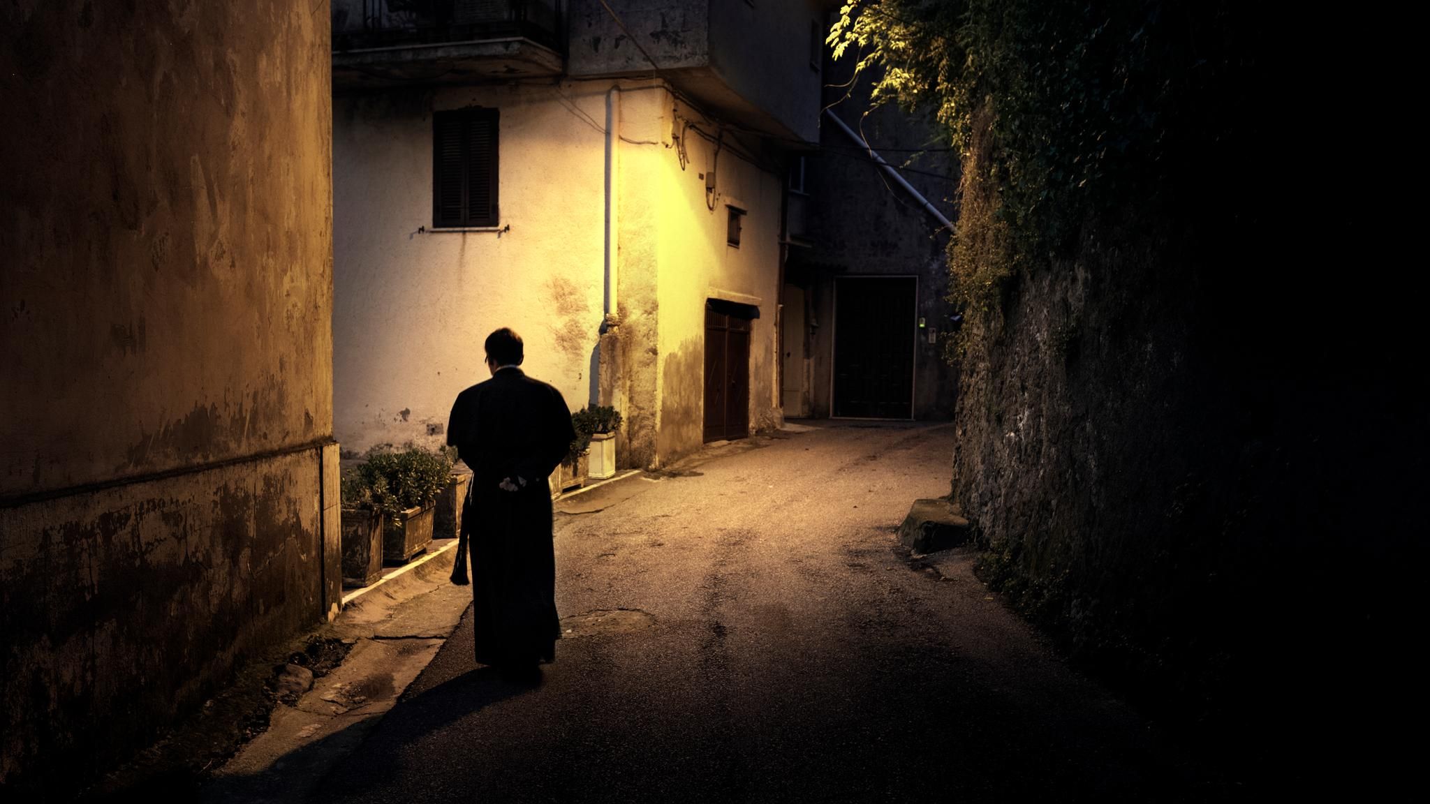 Ein Priester läuft durch eine beleuchtete Gasse