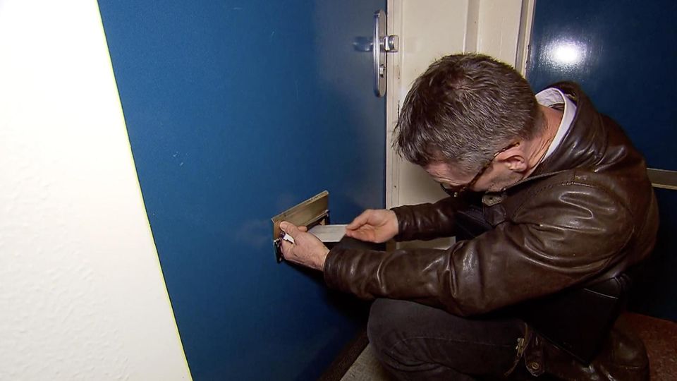 Ein Mann steckt einen Brief durch eine Tür.