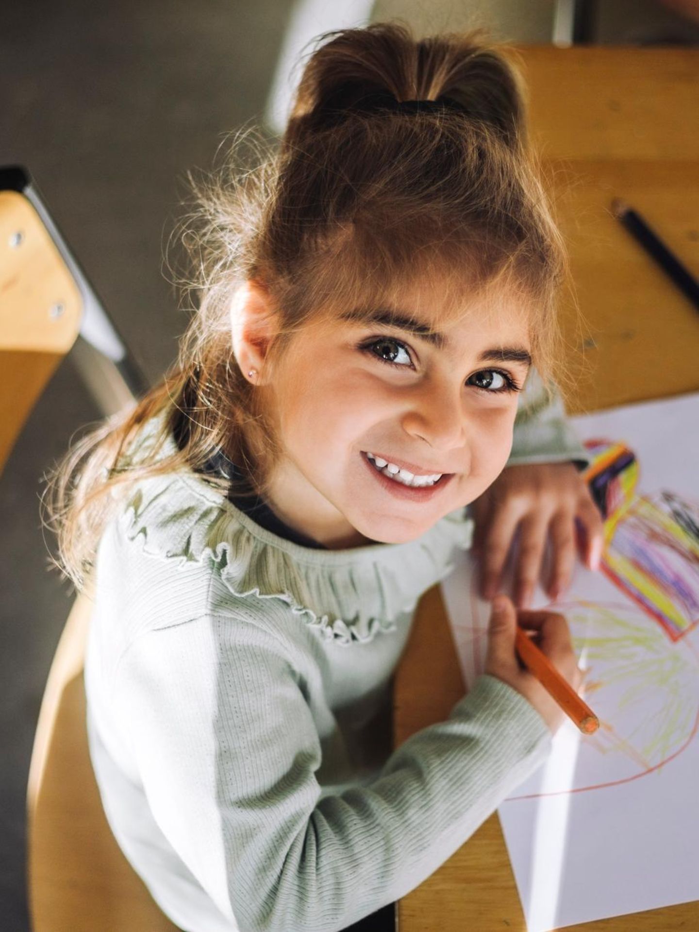 Ein Mädchen sitzt in der Schule und lächelt hoch in die Kamera