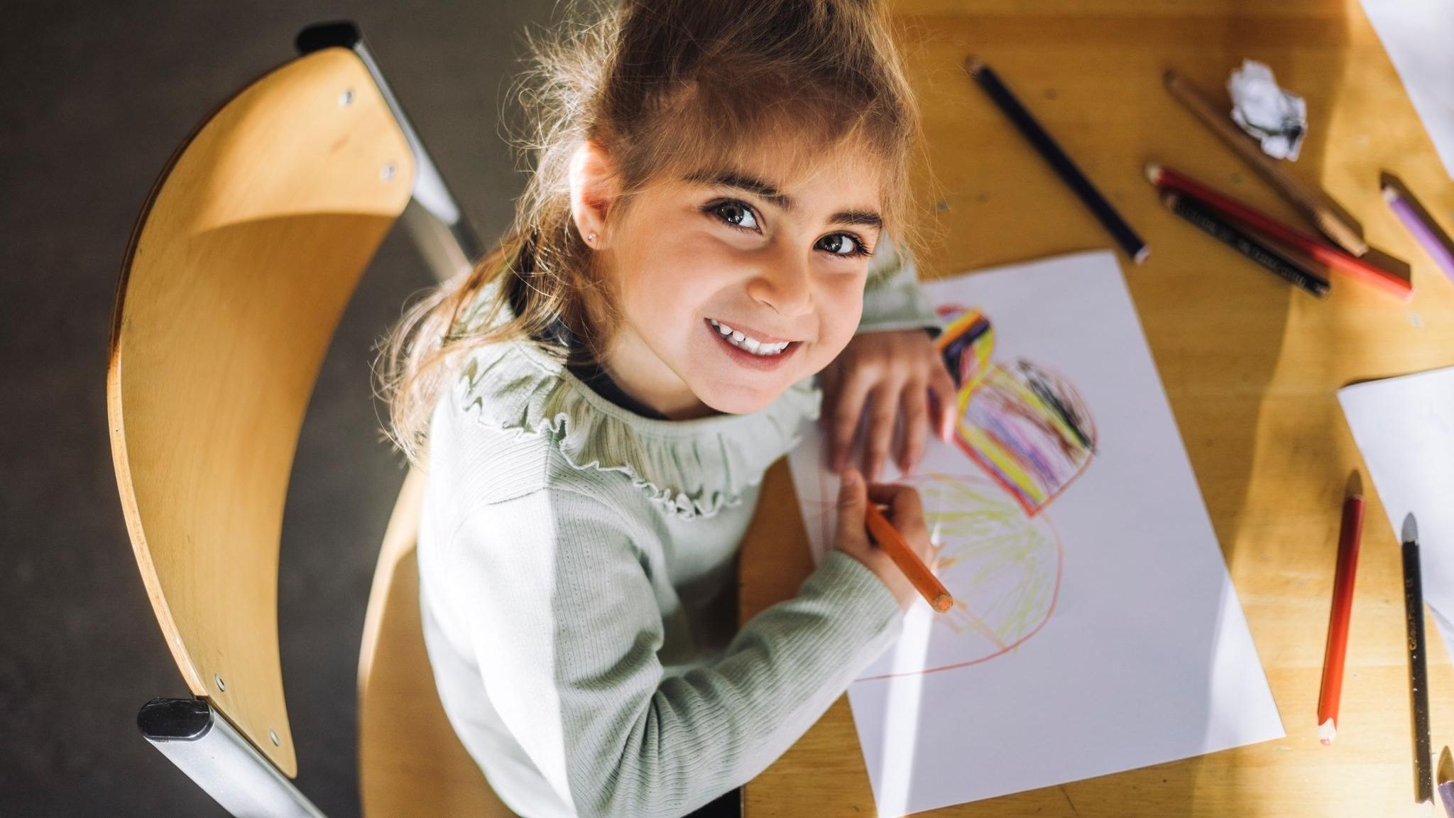 Ein Mädchen sitzt in der Schule und lächelt hoch in die Kamera